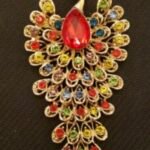 LARGE PEACOCK BROOCH 2'' WIDE X 4'' LONG GOLD-TONE WITH A LARGE RUBY COLORED CENTER STONE AND FULLY DECORATED WITHBRILLANT MULTI COLORED RHINESTONES