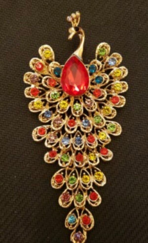 LARGE PEACOCK BROOCH 2'' WIDE X 4'' LONG GOLD-TONE WITH A LARGE RUBY COLORED CENTER STONE AND FULLY DECORATED WITHBRILLANT MULTI COLORED RHINESTONES